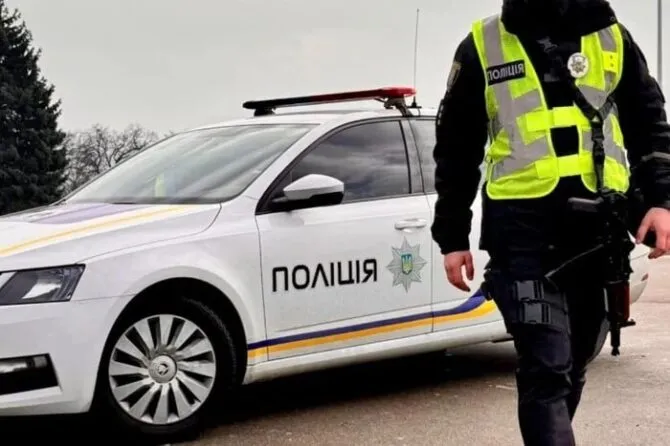 Поліцейський у жовтому жилеті йде біля білого автомобіля поліції