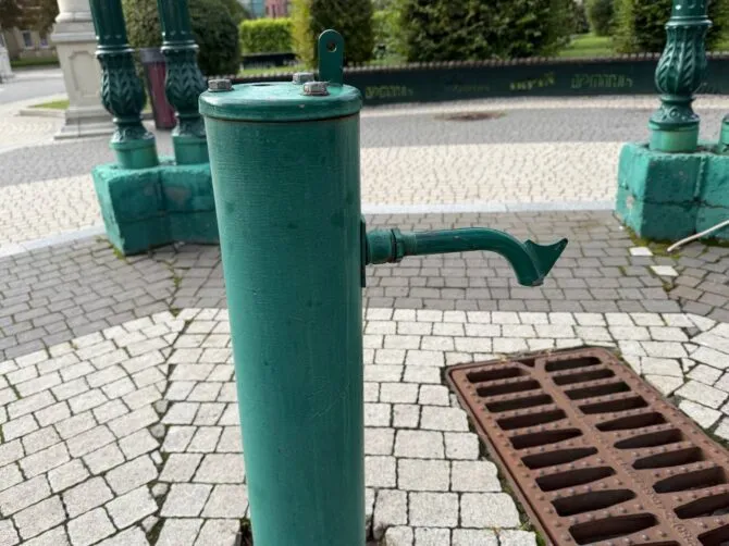 Зелена металева водорозбірна колонка з краном на бруківці площі
