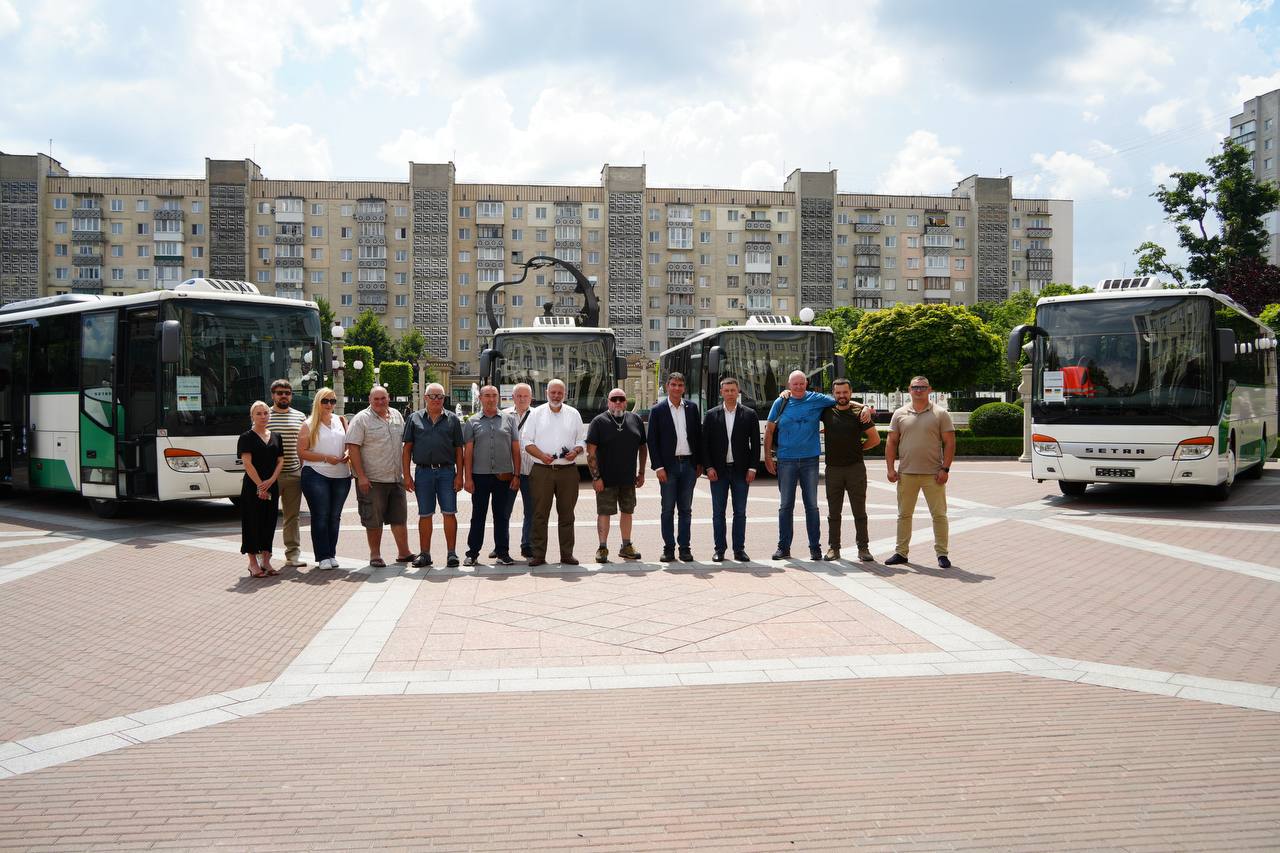 Група людей стоїть на площі перед автобусами Setra та багатоповерхівками