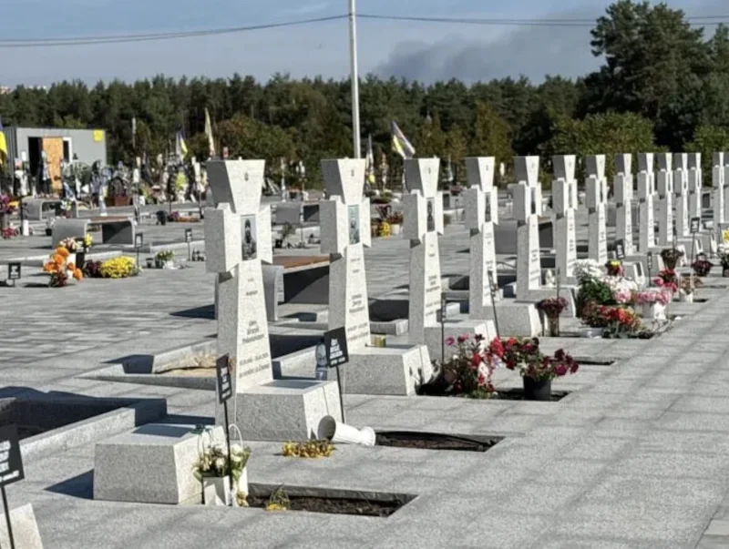 Ряди білих хрестів на військовому цвинтарі з квітами та прапорами