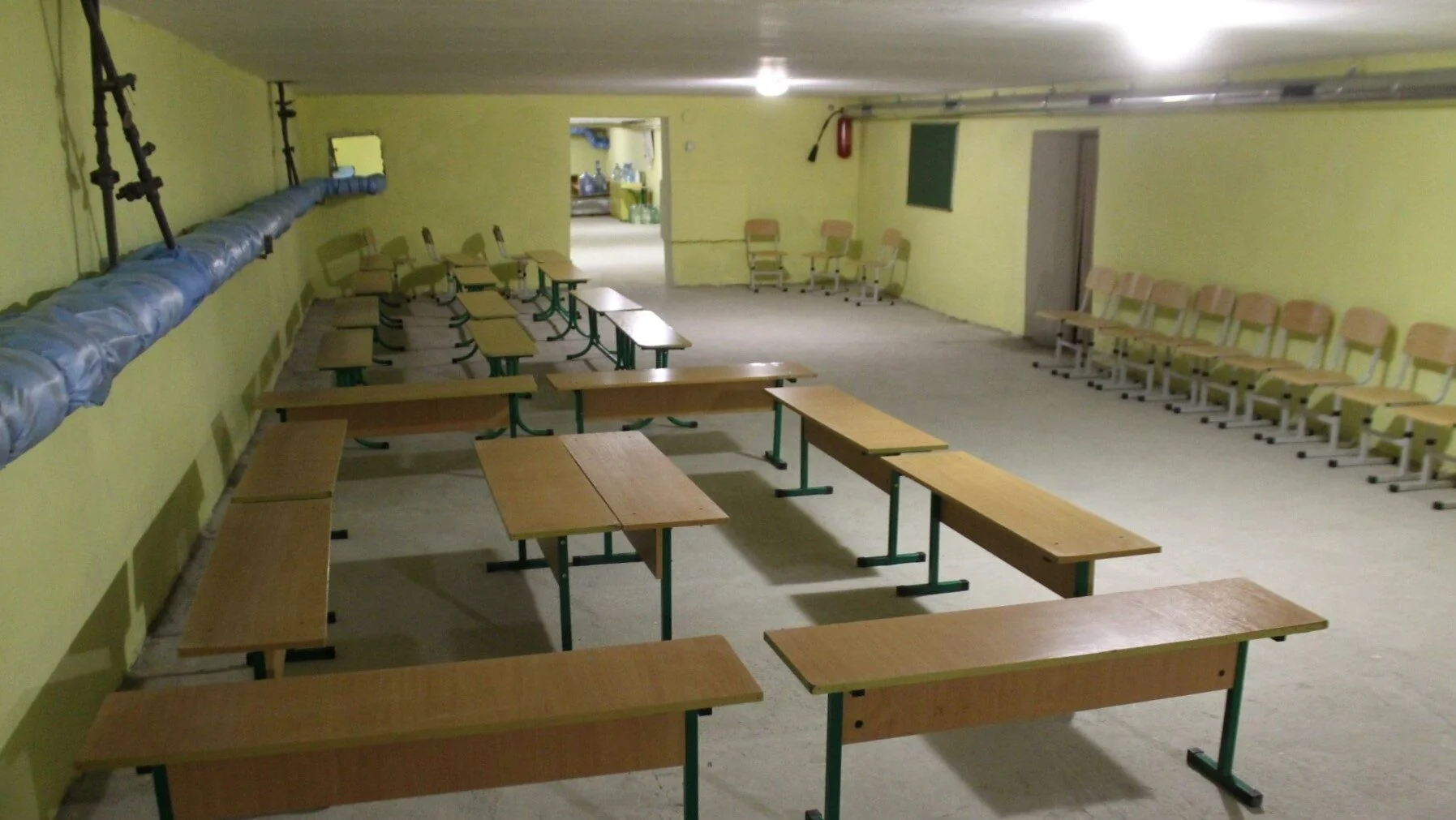 Шкільне укриття з партами та стільцями в підвалі з жовтими стінами